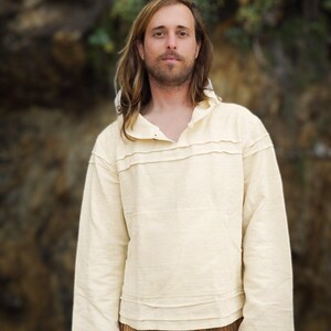 May include: A person wearing a cream-colored, long-sleeved shirt with a hood and a brown and orange patterned pants.