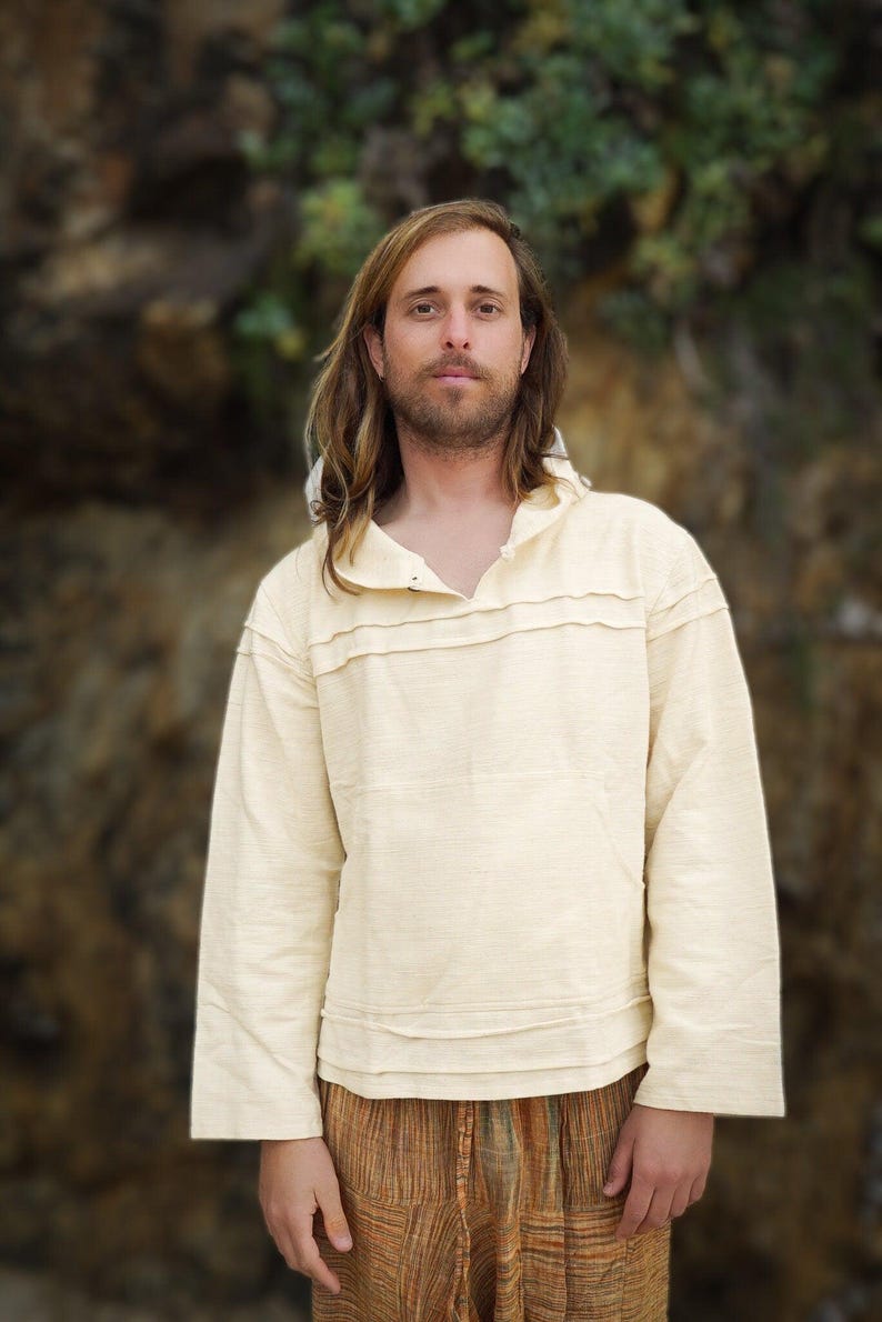 May include: A person wearing a cream-colored, long-sleeved shirt with a hood and a brown and orange patterned pants.