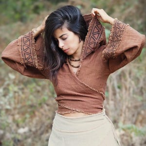 May include: A brown hooded wrap top with geometric patterns and frayed edges. The top is worn over a white wrap skirt.