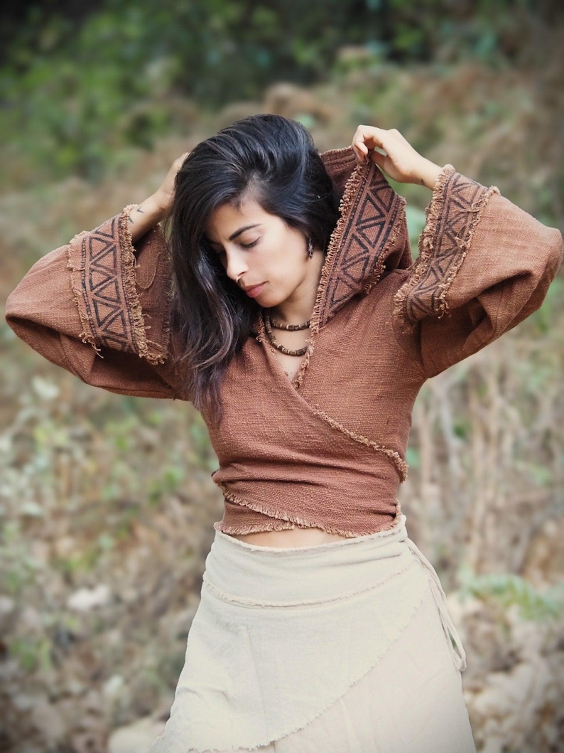 May include: A brown hooded wrap top with geometric patterns and frayed edges. The top is worn over a white wrap skirt.