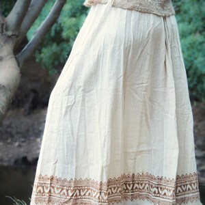 May include: A white cotton skirt with a brown printed border. The skirt has a frayed hem and is flowing.