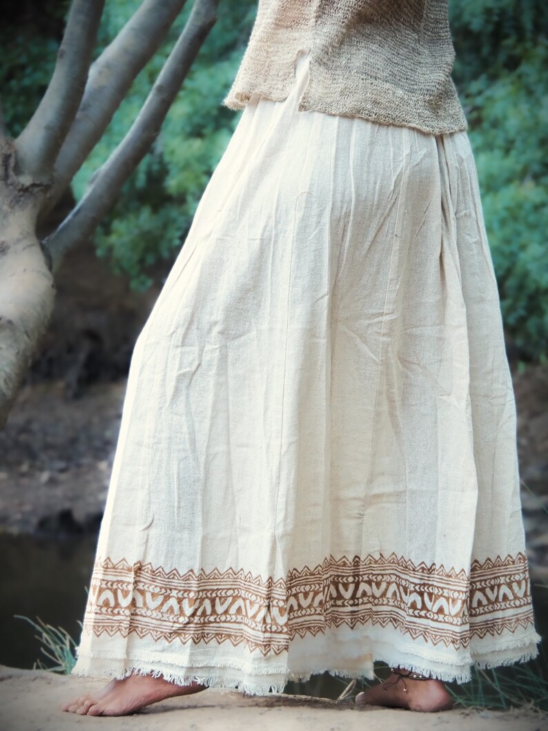 May include: A white cotton skirt with a brown printed border. The skirt has a frayed hem and is flowing.