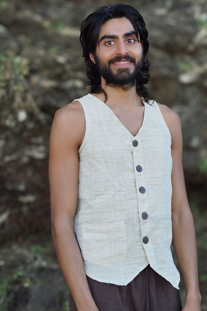 May include: A man wearing a light beige sleeveless vest with brown buttons. The vest has a pocket on the front. The man is wearing brown pants.
