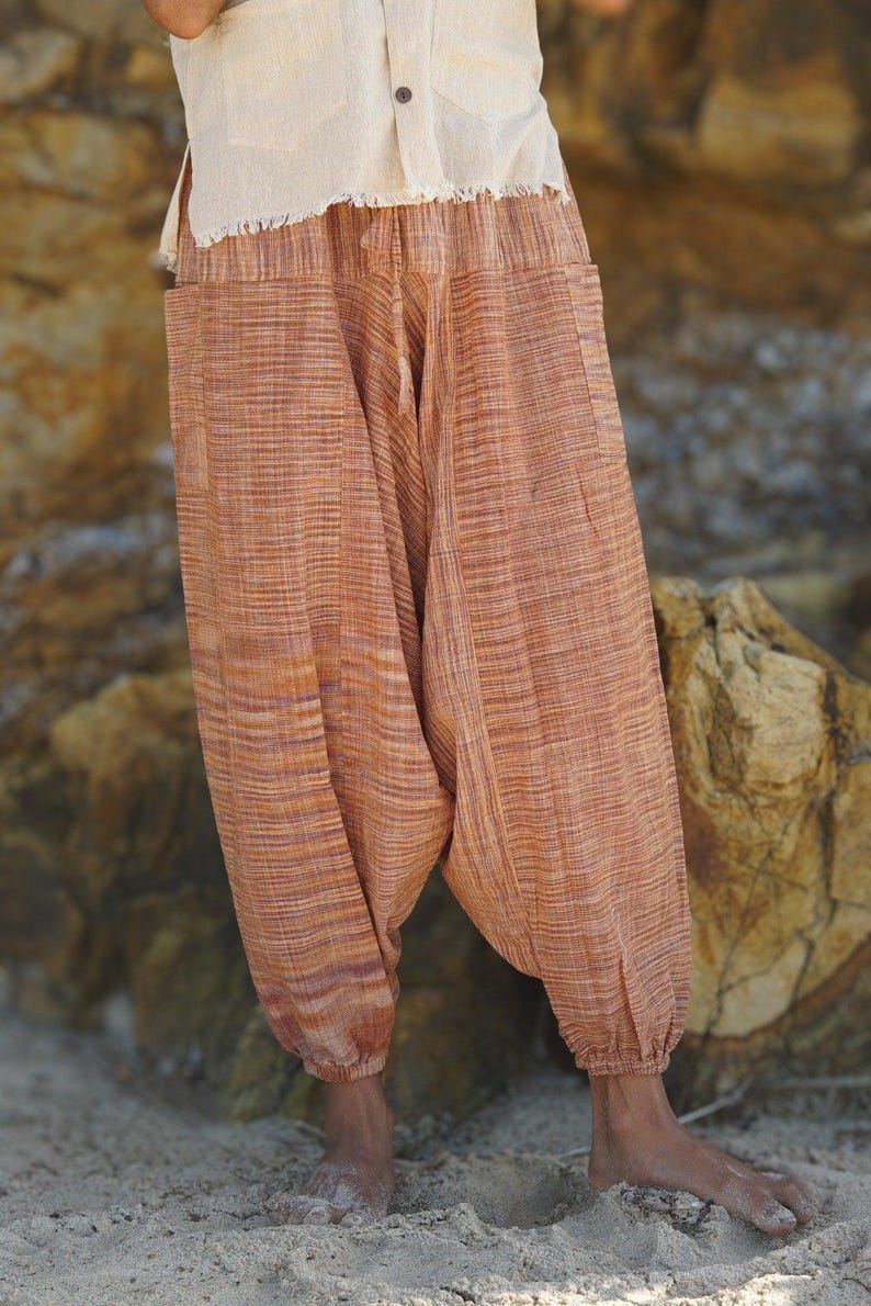 May include: Orange and brown striped harem trousers with pockets. The trousers are made of a lightweight fabric and have elasticated ankles. The top is a cream-coloured, short-sleeved shirt.