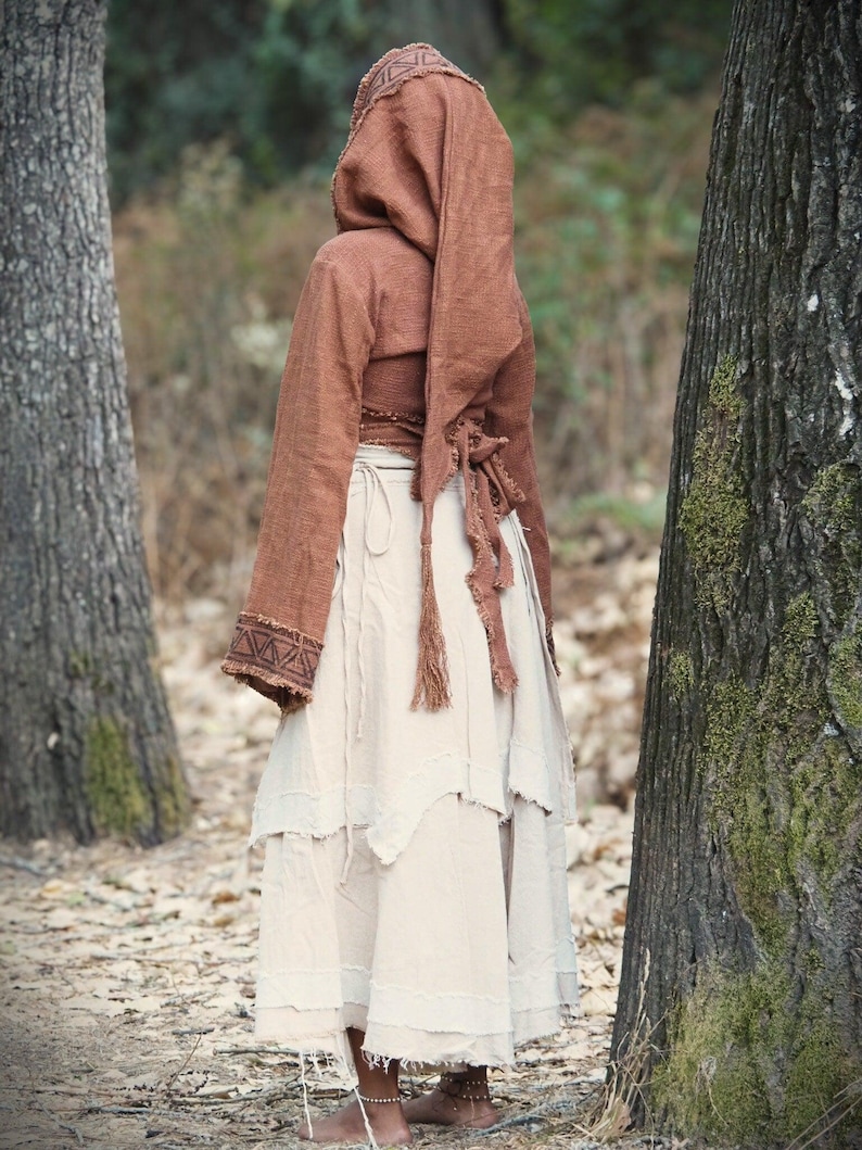 May include: A woman wearing a brown hooded top with a white tiered skirt. The top has a long, flowing sleeve and a cinched waist. The skirt is made of a lightweight fabric and has a frayed hem.