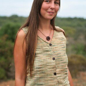 May include: A woman with long brown hair is wearing a sleeveless, light green and brown striped top with a wooden button closure. She is wearing a brown necklace with a wooden pendant.