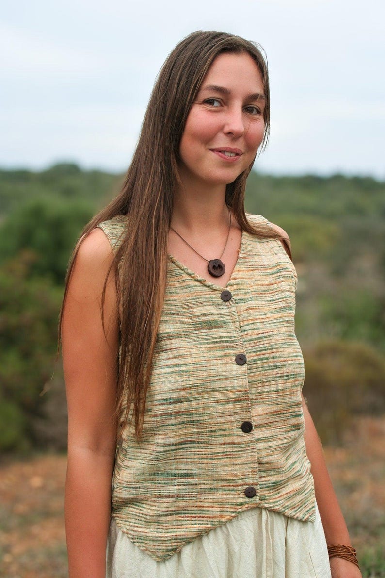 May include: A woman with long brown hair is wearing a sleeveless, light green and brown striped top with a wooden button closure. She is wearing a brown necklace with a wooden pendant.