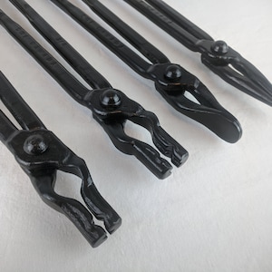 Puede incluir: Cuatro tenazas de herrero de metal negro con diferentes formas de mandíbula. Las tenazas están etiquetadas con sus tamaños: 1/4", 5/16", 3/8", y 1/2".