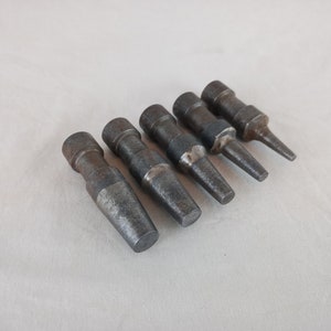 Könnte beinhalten: Fünf Vintage-Metallstempel in verschiedenen Größen und Formen, diagonal angeordnet. Die Stempel haben eine dunkle, verwitterte graue Farbe, die auf Alter und Gebrauch hindeutet. Sie werden wahrscheinlich zum Formen oder Markieren von Materialien verwendet.