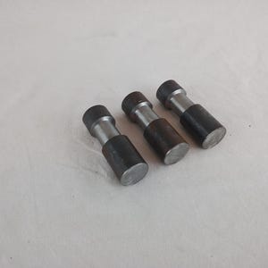 Puede incluir: Tres objetos cilíndricos de metal con extremos de color gris oscuro y una sección central plateada. Están dispuestos en diagonal sobre una superficie blanca. Cada objeto mide unos 5 cm de largo.