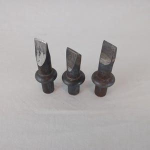 May include: Three metal tools with pointed tips and rounded bases. The tools are silver in color and have a worn, aged appearance.
