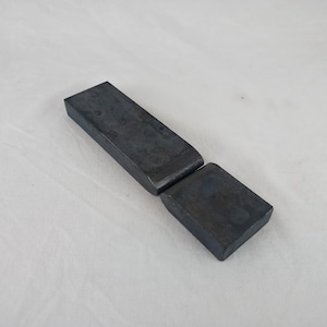 Könnte beinhalten: Zwei Metall-Scharnierteile, eines lang und eines kurz, beide in dunkelgrauer Farbe.