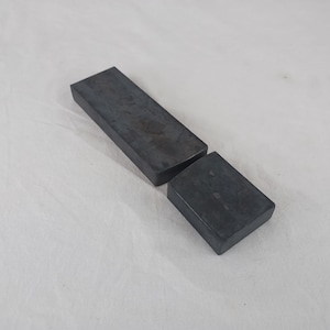 May include: Two rectangular black sharpening stones, one larger than the other, on a white surface.