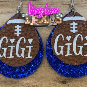 May include: A pair of blue and brown glitter football-shaped earrings with the word "GIGI" and a hashtag on each earring.