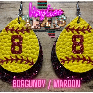 K&ouml;nnte beinhalten: Ein Paar Softball-Ohrringe mit einem burgunderfarbenen und maroonfarbenen Glitzer-Hintergrund. Die Ohrringe sind in Form eines Softballs mit einer roten Nummer 8 auf der Vorderseite. Der Text "BURGUNDY / MAROON" ist unter den Ohrringen gedruckt.
