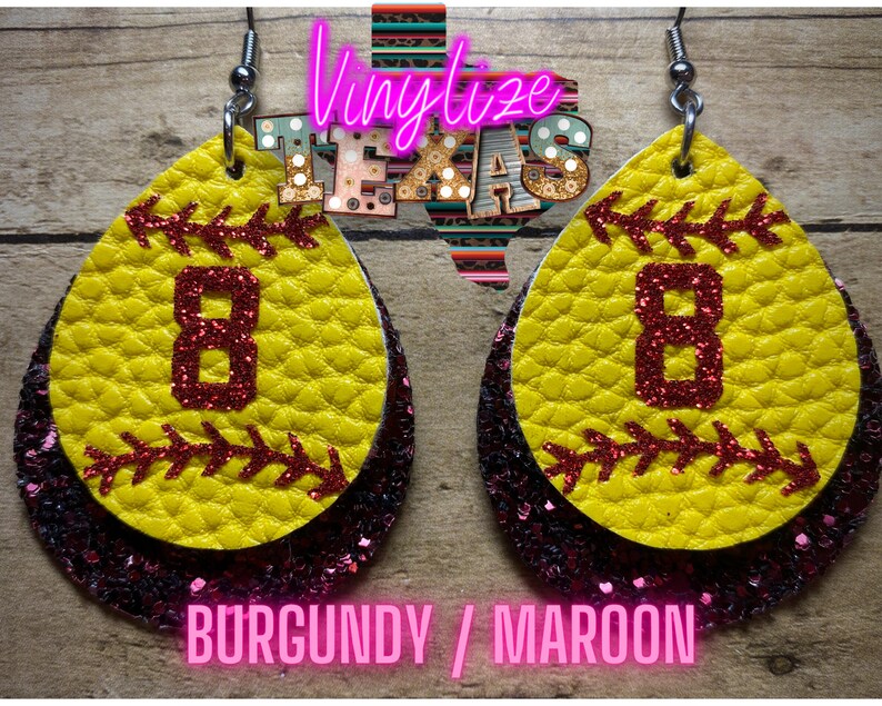 K&ouml;nnte beinhalten: Ein Paar Softball-Ohrringe mit einem burgunderfarbenen und maroonfarbenen Glitzer-Hintergrund. Die Ohrringe sind in Form eines Softballs mit einer roten Nummer 8 auf der Vorderseite. Der Text "BURGUNDY / MAROON" ist unter den Ohrringen gedruckt.