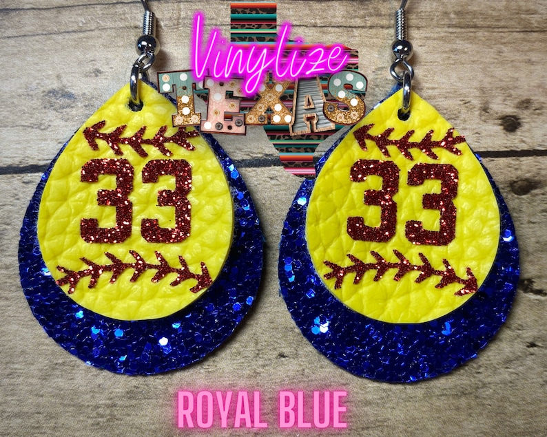 K&ouml;nnte beinhalten: Ein Paar gelbe und blaue Softball-Ohrringe mit der Nummer 33 in rotem Glitzer. Die Ohrringe sind aus Leder und haben eine royalblaue Glitzer-R&uuml;ckseite.
