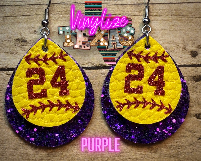 K&ouml;nnte beinhalten: Ein Paar lila und gelbe Softball-Ohrringe mit der Nummer 24 darauf. Die Ohrringe sind aus Leder und Glitzer.