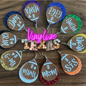 May include: A set of 10 pairs of football-shaped earrings with different glitter colors and names like "Mama", "Grandma", "Sis", and "Mom". The earrings are made of brown leather and have a white glitter finish. The earrings are displayed on a wooden surface with a sign that says "Vinylze Texas".