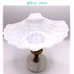 May include: White milk glass seashell-shaped serving dish with a gold metal pedestal and a marble base.  The dish has a scalloped edge and a center dip.  Dots Connection @Etsy store