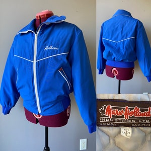 Può includere: Una giacca vintage blu con piping bianco e un nome ricamato in bianco "Arthena". La giacca ha una chiusura a zip e un'etichetta bianca che recita "Mary Holland Industries Ltd. Canada CA04944 M Lady".