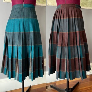 May include: Two pleated skirts on display. One is teal, grey, and brown plaid, the other is brown, grey, and teal plaid. Both skirts are knee-length and have a high waist. The skirts are displayed on dress forms.
