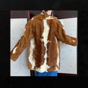 May include: A brown and white cowhide fur coat with a collar. The coat is made of real fur and has a natural pattern.