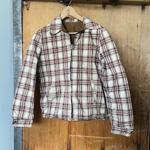 May include: A white, brown, and blue plaid jacket with a zipper closure. The jacket is hanging on a wooden hanger.