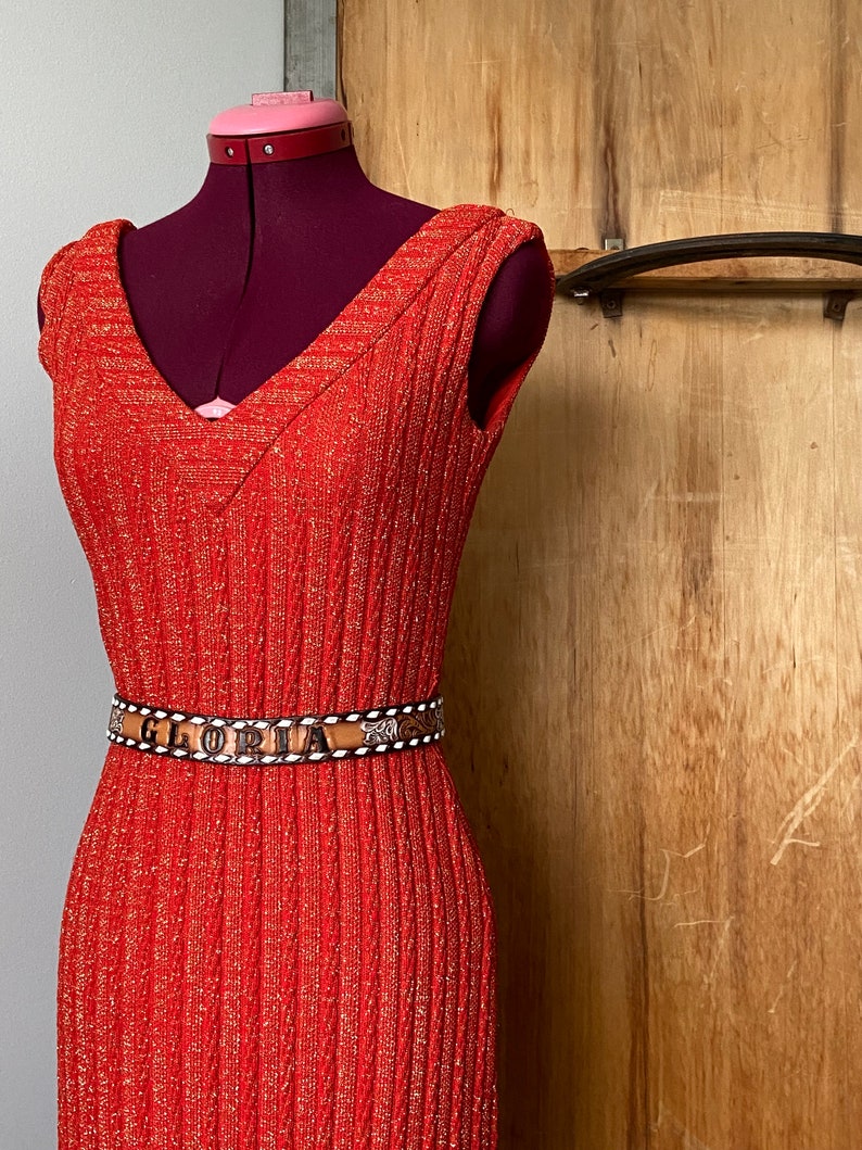 May include: A red sleeveless dress with a sparkly texture and a brown belt with the word "GLORIA" embossed on it.