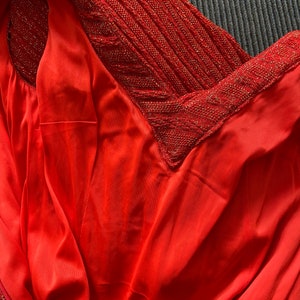 May include: Close-up of a red dress with a sparkly, textured neckline. The fabric is smooth and silky.