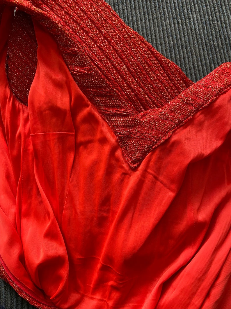 May include: Close-up of a red dress with a sparkly, textured neckline. The fabric is smooth and silky.