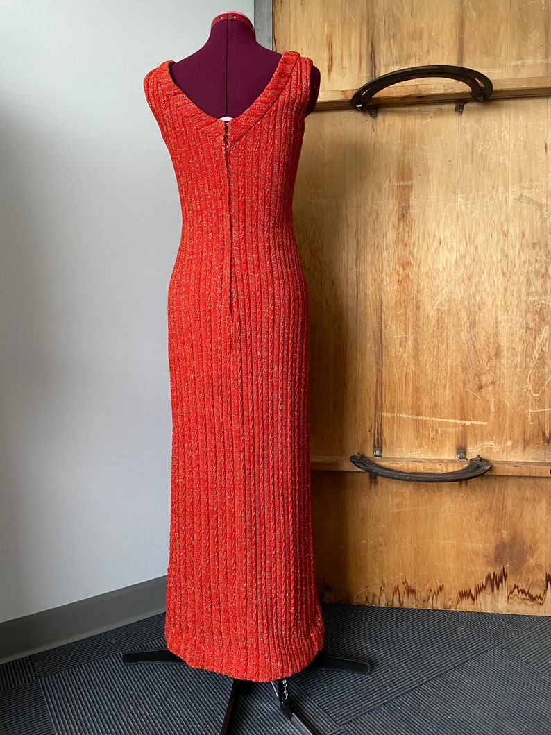 May include: A long, sleeveless, red dress with a V-neckline and a zipper down the back. The dress is made of a textured fabric with a subtle shimmer.