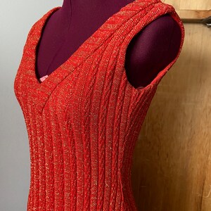 May include: A sleeveless red dress with a v-neck and a sparkly texture.