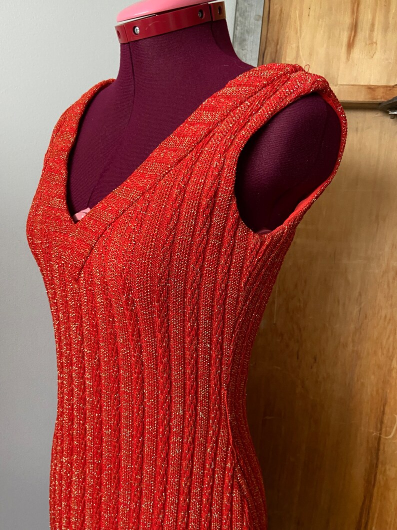 May include: A sleeveless red dress with a v-neck and a sparkly texture.