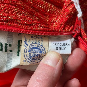 May include: Red knit dress with gold glitter, a zipper, and a white tag that says "DRY CLEAN ONLY". The tag also has a union label that says "ILGWU, Union Made, AFL-CIO, Workers Union".