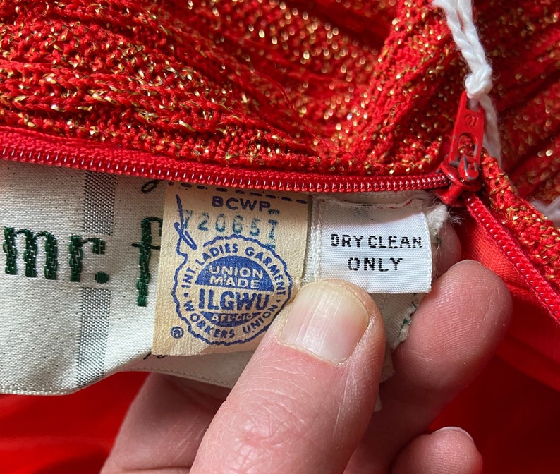 May include: Red knit dress with gold glitter, a zipper, and a white tag that says "DRY CLEAN ONLY". The tag also has a union label that says "ILGWU, Union Made, AFL-CIO, Workers Union".