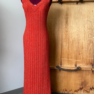 May include: A long, sleeveless, orange dress with a V-neckline and a subtle shimmer. The dress is made of a textured fabric and has a fitted silhouette.
