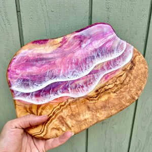 Pode incluir: Uma bandeja de servir de madeira com uma incrusta&ccedil;&atilde;o de resina rosa, branca e dourada. A resina tem um padr&atilde;o de ondas.