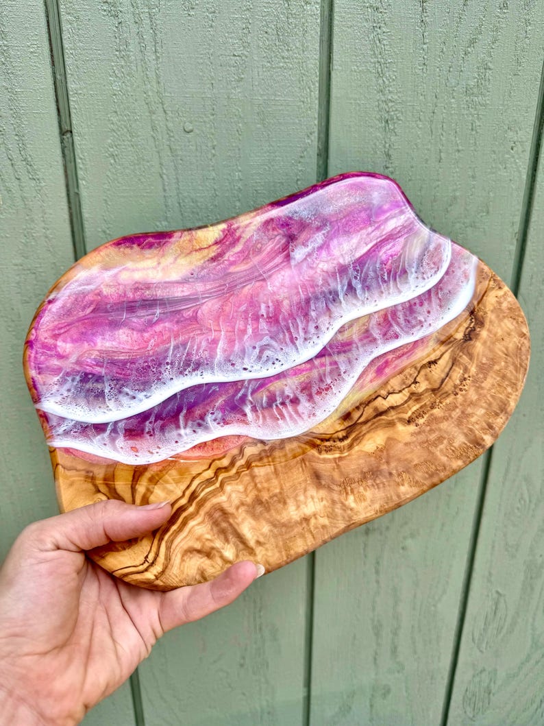 Pode incluir: Uma bandeja de servir de madeira com uma incrusta&ccedil;&atilde;o de resina rosa, branca e dourada. A resina tem um padr&atilde;o de ondas.