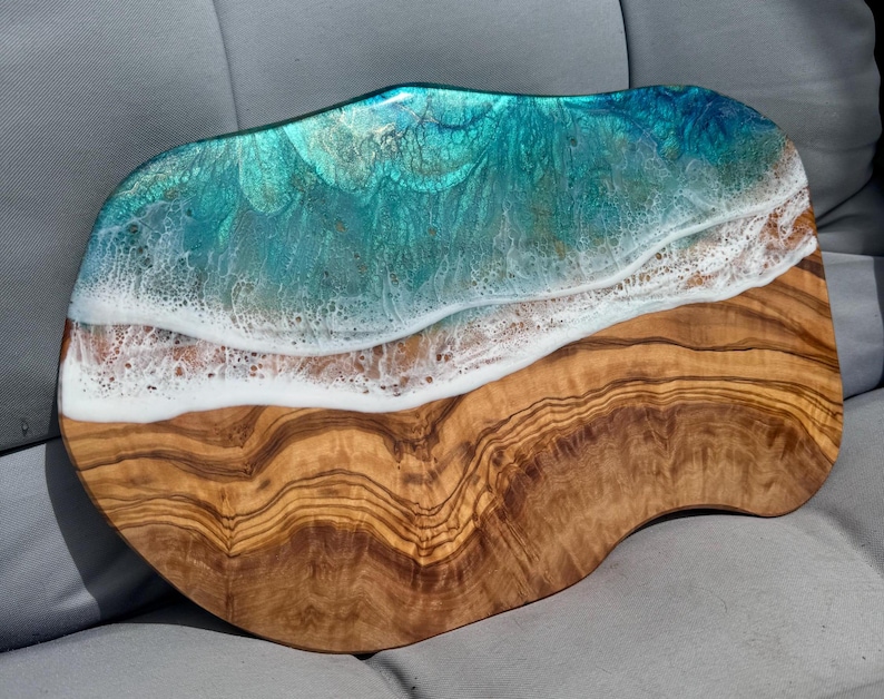 Pode incluir: Uma t&aacute;bua de servir de madeira com um design de resina ep&oacute;xi azul e branco que se assemelha a ondas do oceano. A t&aacute;bua tem um padr&atilde;o de gr&atilde;o de madeira natural e uma forma &uacute;nica e irregular.