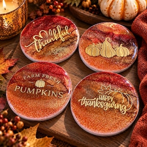 Pode incluir: Quatro porta-copos redondos de resina com acabamento em glitter vermelho, laranja e dourado. Cada porta-copos apresenta texto e gráficos dourados: Thankful, três abóboras, Farm Fresh Pumpkins e Happy Thanksgiving.