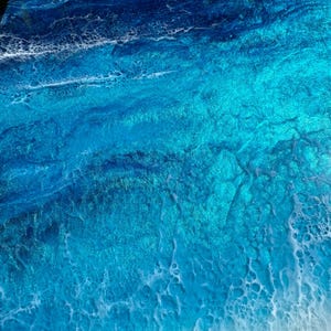May include: Abstract artwork with a coastal theme. The image shows a close-up of a surface with layers of blue and turquoise resin, resembling ocean waves. The resin has a glossy finish with white foamy details.