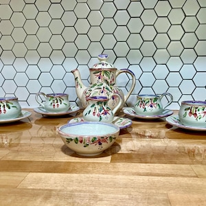 May include: A vintage tea set with a floral design. The set includes a teapot, creamer, sugar bowl, and four teacups and saucers. The teacups and saucers are decorated with a floral pattern in shades of pink, purple, and green.
