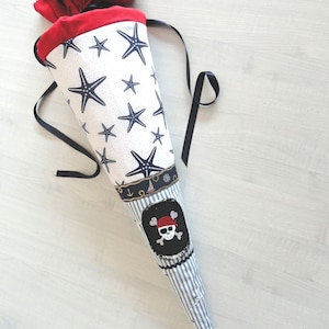 May include: A white and blue striped fabric cone with a red and white fabric pirate skull patch. The cone has a black ribbon and is decorated with white starfish and anchors.