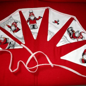 May include: A red and white fabric garland with a Christmas theme. The garland features a repeating pattern of Santa Claus figures in various poses, including holding a pickaxe, carrying a sack, and wearing a hat. The garland is perfect for decorating a home or party for the holidays.