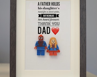 May include: A framed print with a quote about a father's love for his daughter. The quote reads "A father holds his daughter's hand for a short while, but he holds her heart forever. Thank you Dad." The print features two Lego minifigures, one of Spider-Man and one of a female superhero.