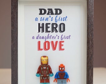 May include: A framed print with the text "DAD a son's first HERO a daughter's first LOVE" and two Lego minifigures, one of Iron Man and one of Spider-Man.