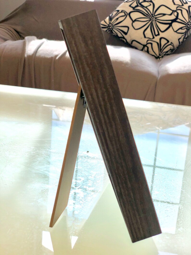 May include: A dark brown wooden picture frame with a stand on the back. The frame is standing on a glass table.
