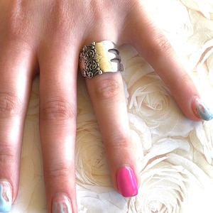 May include: A silver fork ring with a decorative design. The ring is worn on a finger with blue and pink nail polish.