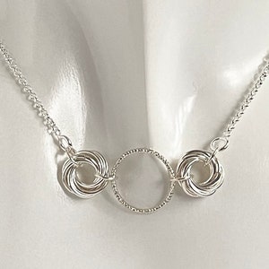 May include: Silver necklace with three interconnected circles. The center circle is plain, while the two outer circles are made of multiple intertwined rings.